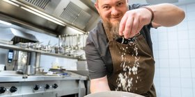 Vielseitigkeit in der Gastronomie Der Sous Chef streut Parmesan auf einen Teller mit Spaghetti in der Küche des Freiwerks.